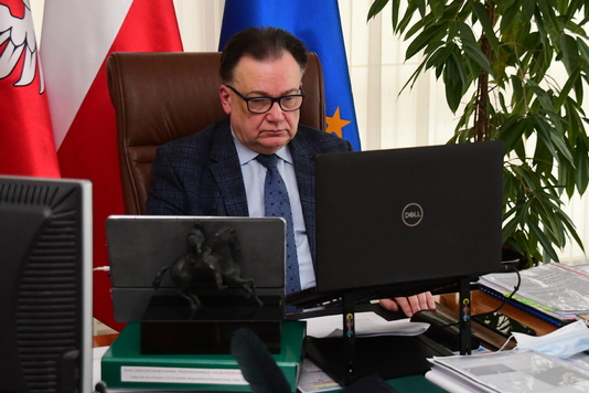 Marszałek Adam Struzik siedzi za biurkiem w swoim gabinecie. Wpatruje się w monitor, obok leży otwarty ekran. W tle widać flagi Unii Europejskiej, Polski i flaga z godłem województwa