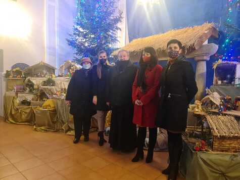 Członek zarządu Janina Ewa Orzełowska stoi w rzędzie wraz z innymi członkami komisji konkursowej. Pozują do zdjęcia. Obok nich, w tle widać szopki