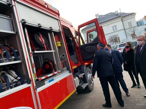 Bok samochodu strażackiego z otwartymi schowkami na sprzęt. Marszałek zagląda do wnętrza auta