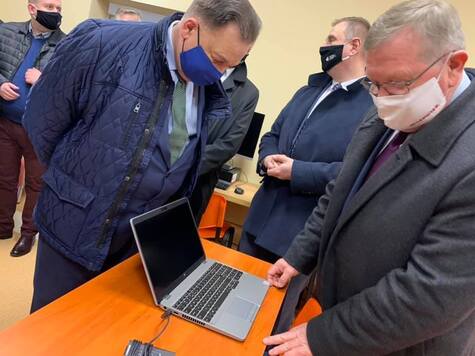 Marszałek i radny Przybytniak oglądają laptopa, rozłożonego na jednej ze szkolnych ławek