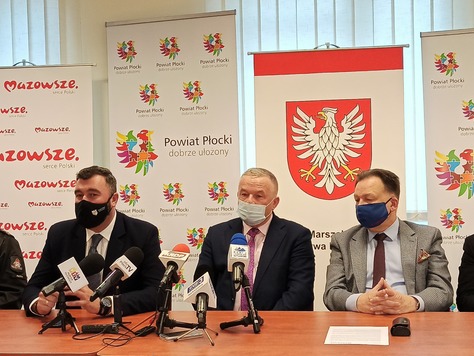 Trzech mężczyzn, m.in. marszałek Struzik, siedzą obok siebie przy stole konferencyjnym. Przed nimi stoją mikrofony ze stacji radiowych