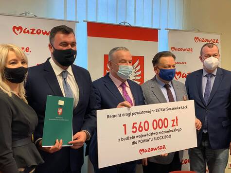 Marszałek, wicemarszałek oraz trzech beneficjentów (dwóch mężczyzn i kobieta) stoją obok siebie i pozują do zdjęcia. Marszałek i stojący obok beneficjent trzymają tablicę z kwotą na modernizację drogi