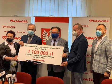 Marszałek, wicemarszałek, dyrektor płockiej delegatury oraz dwóch beneficjentów stoją obok siebie i pozują do zdjęcia. Beneficjenci oraz marszałek trzymają razem tablicę z kwotą przeznaczoną na budowę i remont ulic