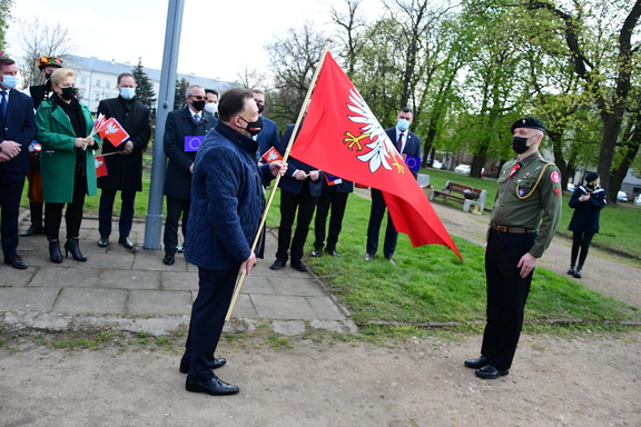 Elegancko ubrany mężczyzna trzyma flagę Mazowsza- przed nim stoi żołnierz w mundurze