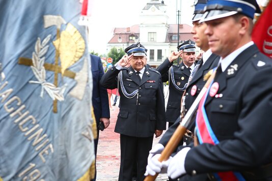 kilku mężczyzn w galowych mundurach strażackich, jeden z nich trzyma sztandar jednostki