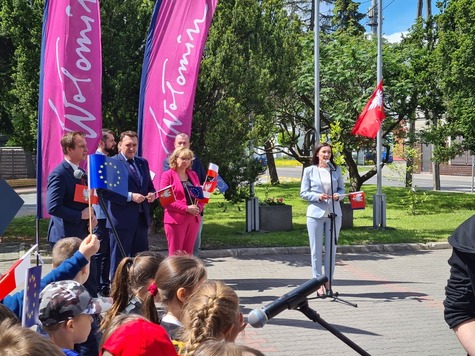 Grupa osób stoi pod flagą z napisem Wołomin, jedna kobieta przemawia