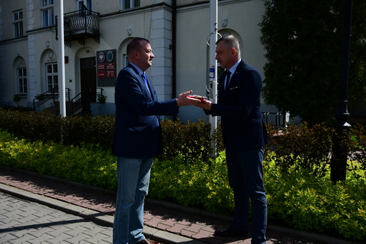 Jeden mężczyzna w garniturze przekazuje drugiemu mężczyźnie flagę Mazowsza