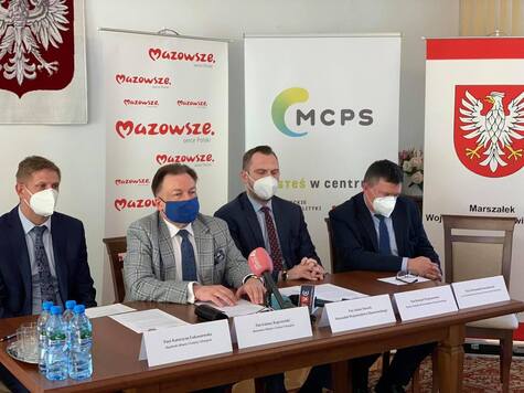 Czterech mężczyzn siedzi przy stole, w tle ścianki MCPS