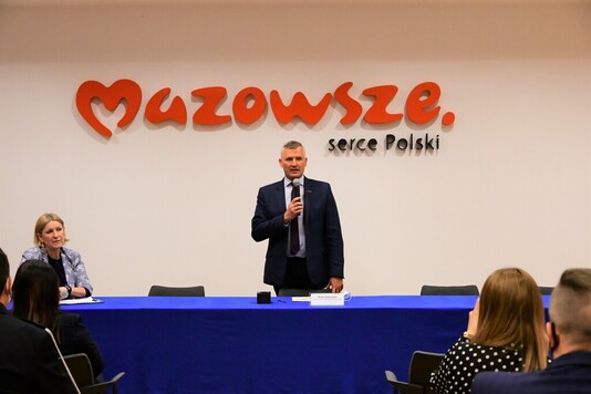 Mężczyzna z mikrofonem, w tle logo Mazowsze Serce Polski.