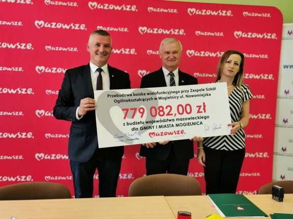 Dwóch mężczyzn i kobieta stoją i trzymają w rękach czek na 779 tys. zł.