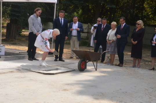 Kobieta w białej sukience zamurowuje akt erekcyjny, obok stoja pozostali zebrani