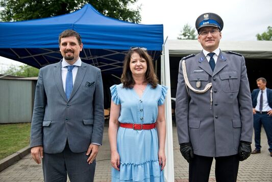 Policjant w galowym mundurze, kobieta i mężczyzna w cywilnym garniturze stoją obok siebie i pozują do zdjęcia