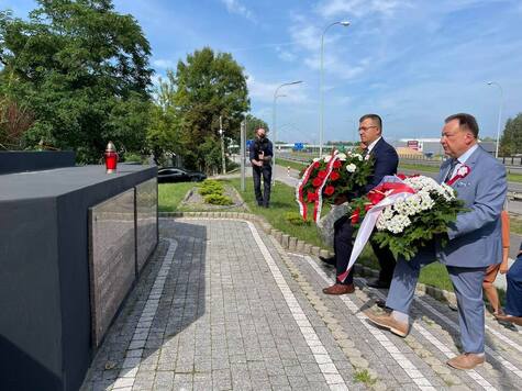 Dwóch samorzadowcow podchodzi z wieńcami pod pomnik