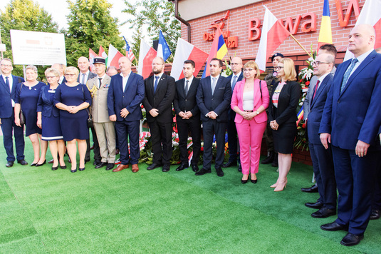 Uczestnicy uroczystości w Ossowie stoją w rzędzie pozując do pamiątkowego zdjęcia.