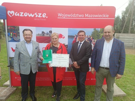 Zdjęcie pamiątkowe. Grupa osób z dyplomami pamiątkowymi na tle ścianki promocyjnej.