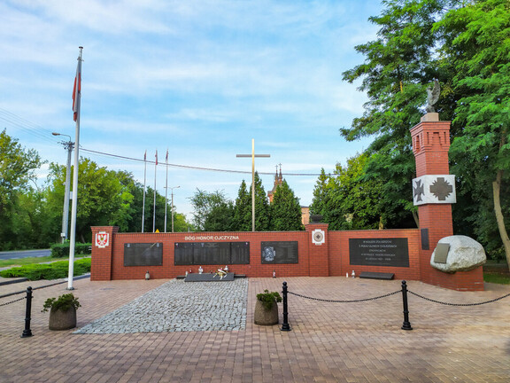 Miejsce pamięci. Mur z cegły z centralnie umieszczonym krzyżem,   na murze umieszczone są pamiątkowe tablice. Po prawej stronie cokół zwieńczony wizerunkiem orła z rozpostartymi skrzydłami.