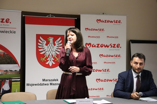 Kobieta mówi przez mikrofon na tle ścianek promocyjnych.