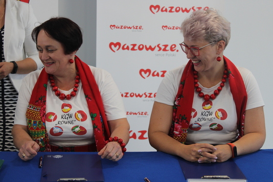 Dwie kobiety z koła gospodyń wiejskich siedzą za stołem konferencyjnym, uśmiechają się