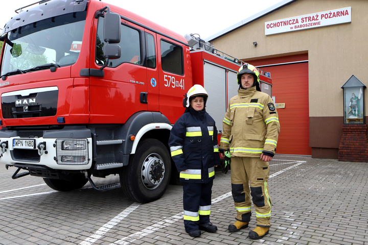 Kobieta i mężczyzna w uniformach strażackich na tle samochodu gaśniczego