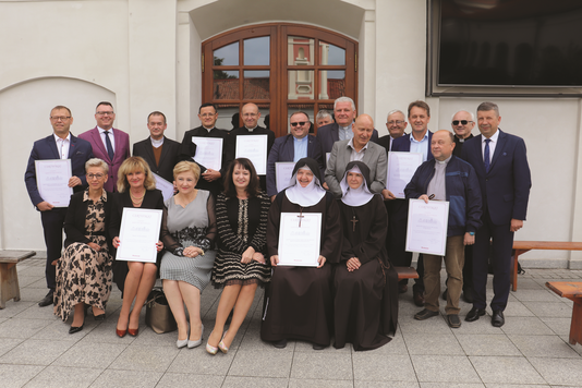 Grupa osób świeckich i zakonnych ustawiona w dwóch rzędach. Niektóre osoby trzymają przed sobą kartki z certyfikatami