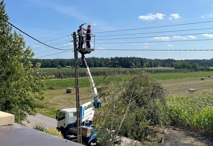 Dwaj robotnicy montują energooszczędną lampę na słupie. Stoją na rampie na podnośniku