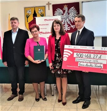 dwaj mężczyźni i dwie kobiety pozują do zdjęcia z czekiem. Mężczyzna trzyma czek, a kobieta teczkę z listem gratulacyjnym