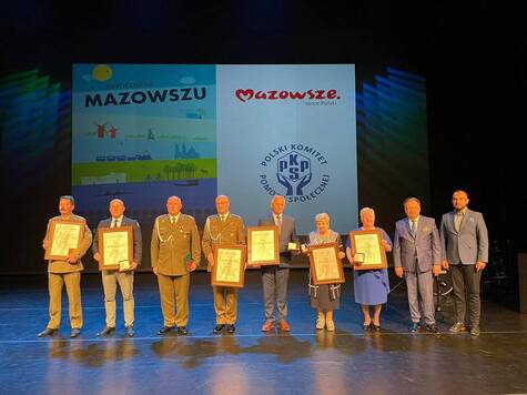 Dziewięcioro osób stoi obok siebie w rzędzie na scenie i pozują do zdjęcia. Wśród nich jest marszałek. Niektórzy trzymają przed sobą dyplomy. 