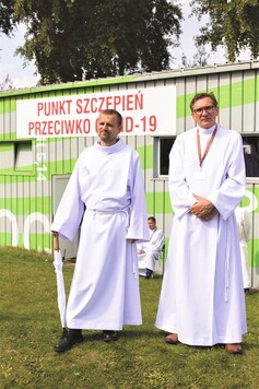 Dwóch księży w strojach liturgicznych prze punktem szczepień