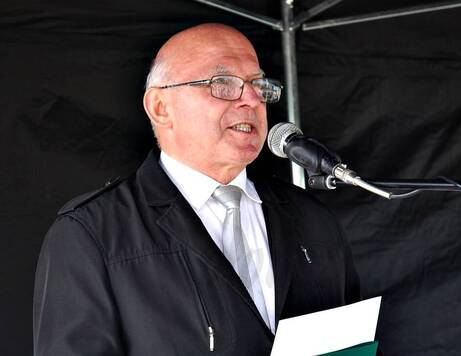Mężczyzna w okularach i garniturze przemawia do mikrofonu. Zdjęcie z bliska