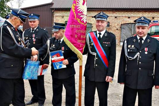 Strażacy w galowych mundurach stoją wraz ze sztandarami w szeregu. Oprócz okolicznościowych medali strażacy otrzymali również flagę Mazowsza.