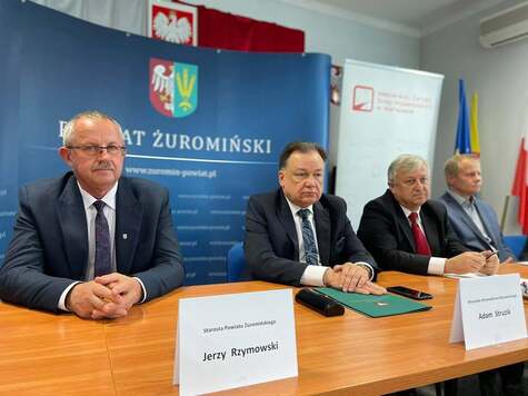 Czterech mężczyzn siedzi za stołem konferencyjnym. Marszałek, który siedzi jako drugi, obok starosty, opiera dłonie o blat. Przed sobą ma teczkę