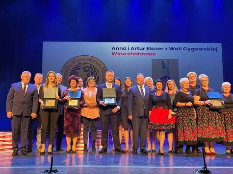 Grupa osób na scenie pozuje z pamiątkowymi dyplomami.