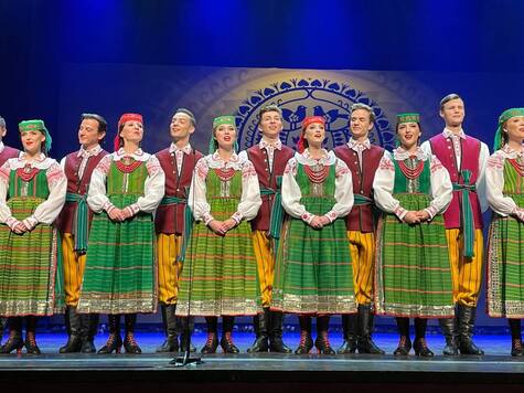 Grupa osób w ludowych strojach tańczy i śpiewa.