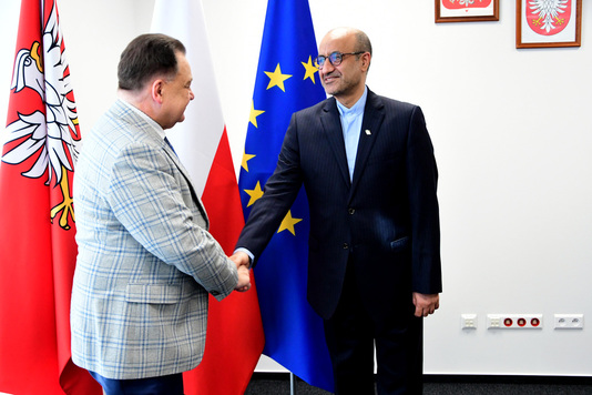 Mraszałek i przedstawiciel Iranu podają sobie ręce na tle flag Mazowsza, Polski i UE