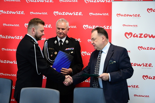 Nagrodzony strażak odbiera z rąk marszałka Struzika List gratulacyjny. Obok nich stoi komendant straży