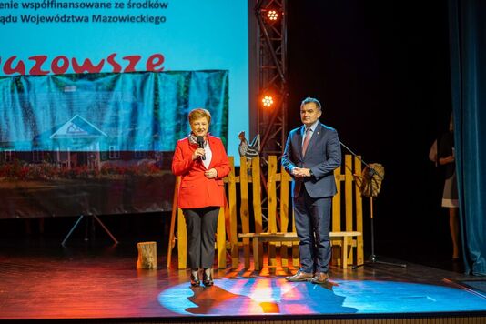 Elżbieta Lanc stoi na scenie z mikrofonem w dłoni. Obok niej stoi mężczyzna w garniturze