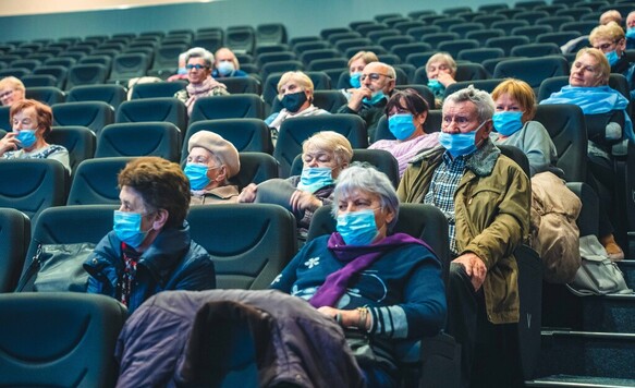 Na widowni dużej sali siedzą seniorzy, wszyscy mają na twarzach maseczki.