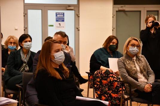 Na widowni na krzesłach siedzą uczestnicy konferencji. Wszyscy są w maseczkach