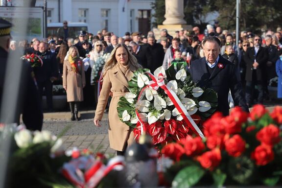 Marszałek Adam Struzik wraz z kobietą w płaszczu składają wieniec biało-czerwonych róż pod pomnikiem