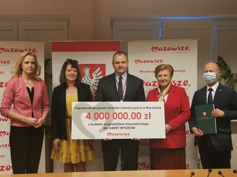 Elżbieta Lanc, Janina Ewa Orzełowska i radna Joanna Bala pozują do zdjęcia z beneficjentami z gminy Wyszków, którzy trzymają symboliczny czek