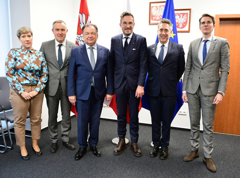 Marszałek i delegacja z Brukseli pozują do zdjęcia na tle flag