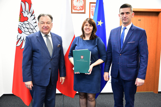 Marszałek, wójt i skarbnik pozują do zdjęcia na tle flag