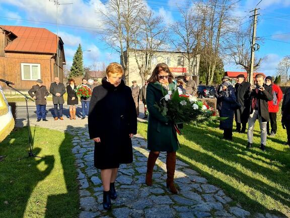 Dwie kobiety z wiązanką kwiatów idą w stronę pomnika powstańców styczniowych