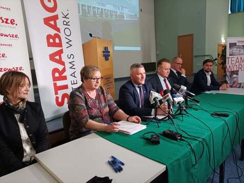 Grupa kobiet i mężczyzn siedzą przy stole i podpisują umowę