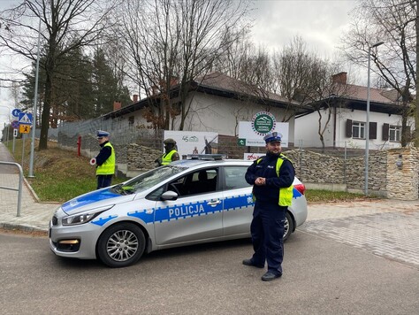 Wóz policyjny, obok stoją funkjonariusze Policji