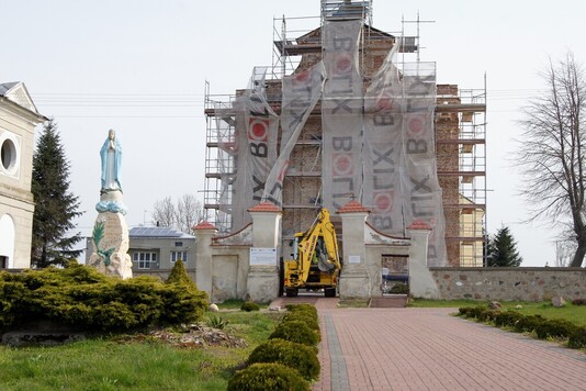 Kościół w trakcie renowacji. Przed główną elewację stoją rusztowania, zaciągnięte siatką ochronną