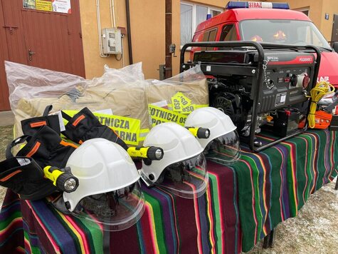 Na stole leżą chełmy i odzież ochronna oraz agregat