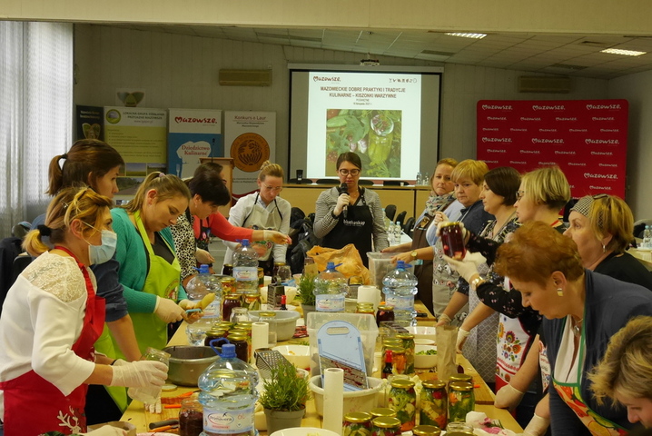 Przy stole gęsto zastawionym warzywami stoją gospodynie w fartuchach, które pracują nad potrawami