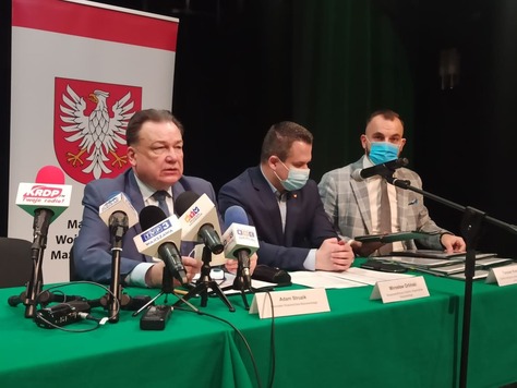 Marszałek, radny Orliński i dyrektor Kominek siedzą po jednej stronie stołu konferencyjnego. Przed nimi są ustawione mikrofony