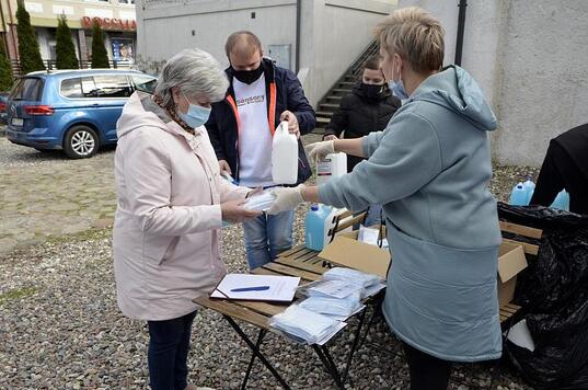 Stanowisko obsługi seniorów, kobieta wręcza seniorce paczkę maseczek